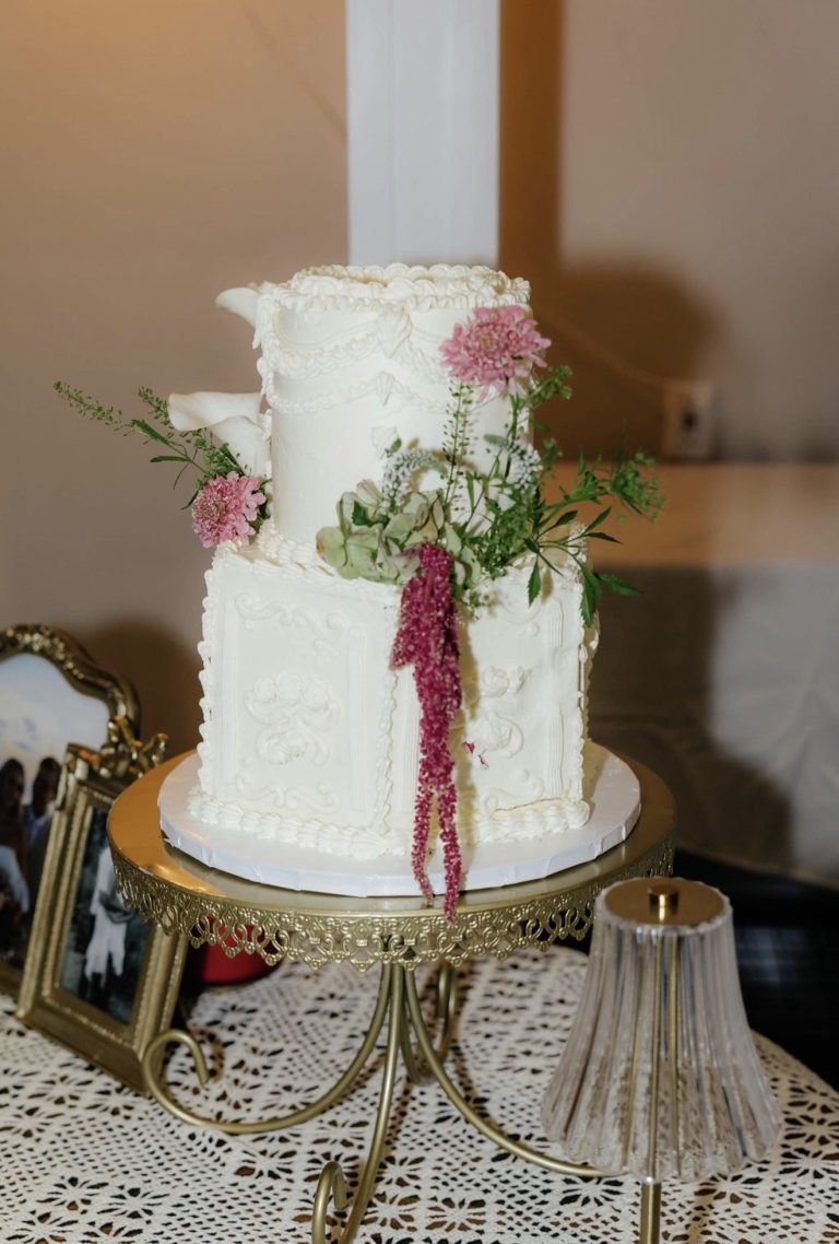 White wedding cake decorated with fresh flowers and hanging amaranthus