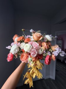 Hand-held bouquet of coral, pink and golden blooms