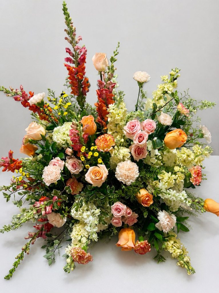 Large arrangement of snapdragons, roses and ranunculus in orange and pink