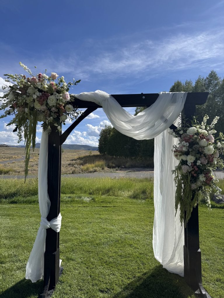 Outdoor wedding arch draped in white fabric with floral corners