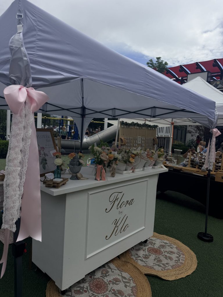 Flora by Klo flower cart with pink ribbon under a white tent at an outdoor market